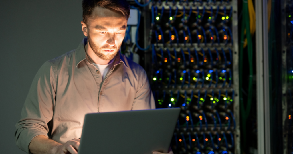 man standing at a laptop in a server room.